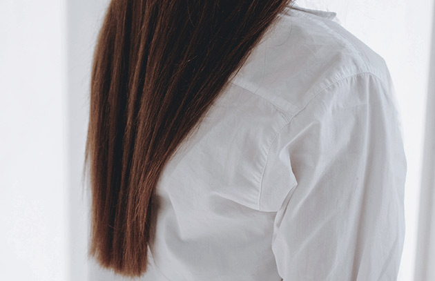 kvinna med långt brunt hår mot en vit vägg